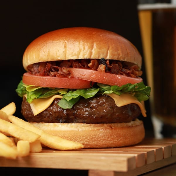 A Da Silva Steakhouse burger with bacon, tomato, lettuce, cheese, and fries on a wooden board.