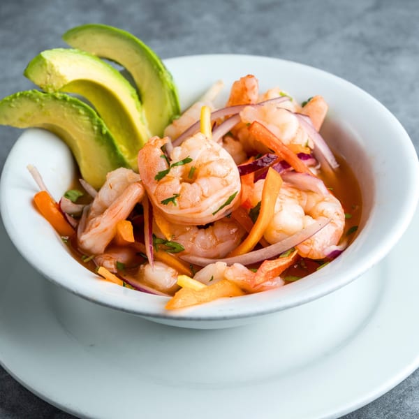 Shrimp ceviche with avocado slices, red onion, and bell peppers in a white bowl.