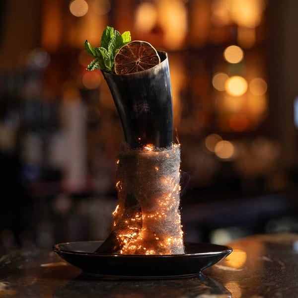 A smoking cocktail in a horn-shaped glass, garnished with mint and a dried orange slice.